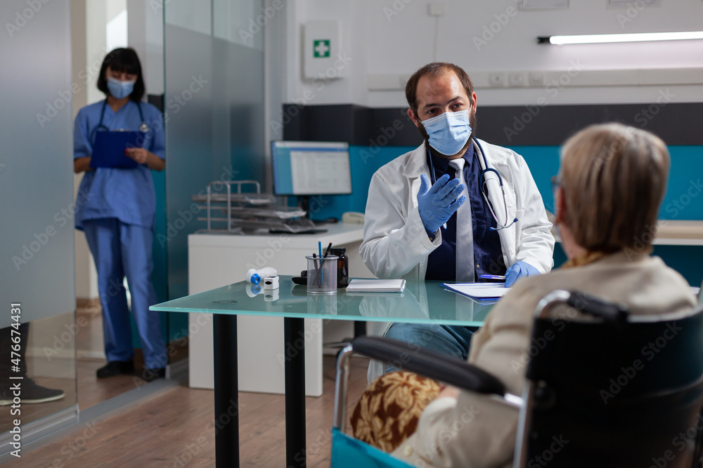 Obraz premium Medic meeting with elder woman sitting in wheelchair at checkup visit, doing health care consultation. Senior patient with physical disability asking for medical advice from physician.