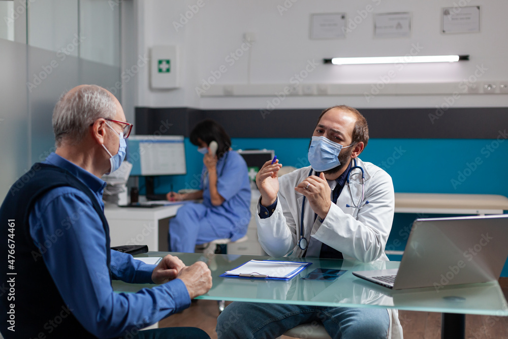 Obraz premium Retired man and physician talking about health care medicine at checkup appointment. Specialist with face mask giving medical advice and assistance to elder person at examination.