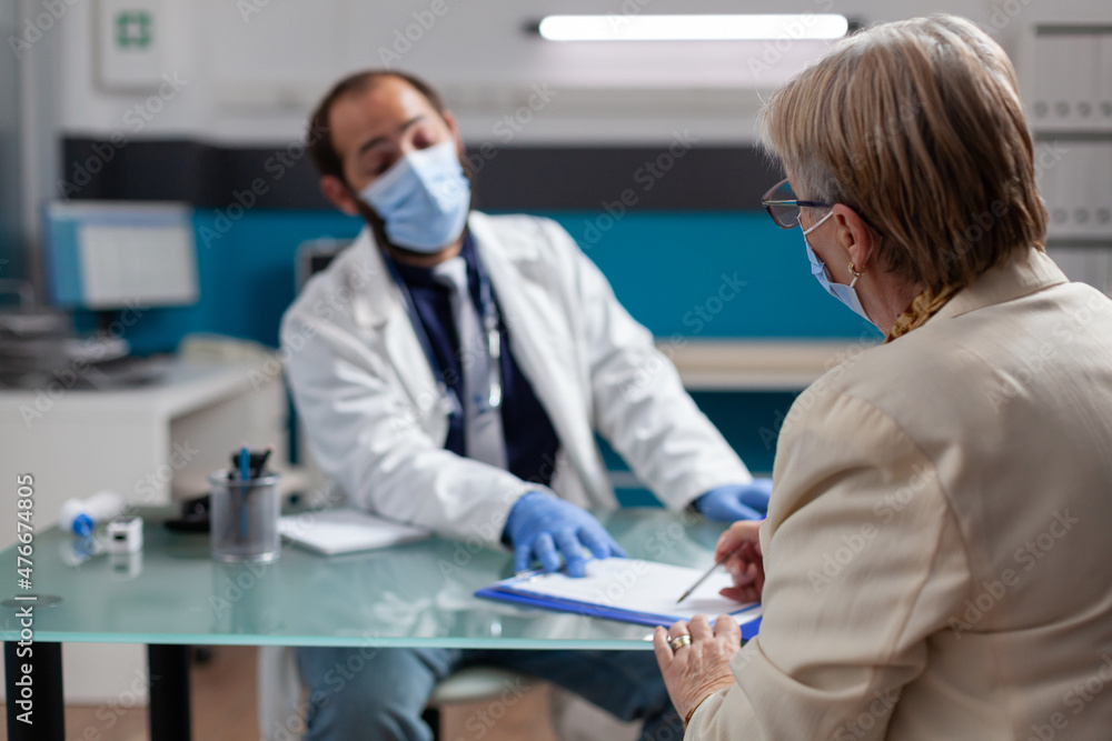 Senior patient signing checkup papers to receive prescription medicine at consultation with doctor. Man with face mask asking for signature to give health care treatment after examination. Senior patient signing checkup papers to receive prescription medicine at consultation with doctor. Man with face mask asking for signature to give health care treatment after examination.
