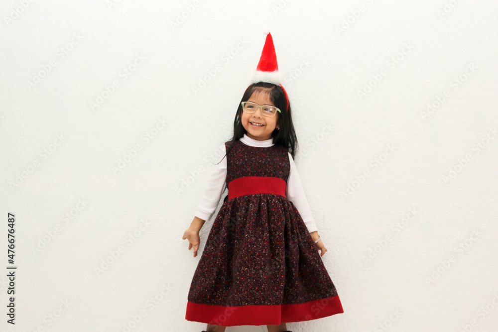 Latin little girl with elegant party dress and Christmas hat dances with happiness for the arrival of December and celebrate Christmas the new year
