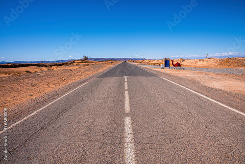 Asphalt road with white markings through sandy desert under blue sky, Narrow asphalt road with markings