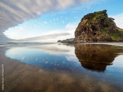 View of Piha Beach, Auckland, New Zealand with Lion Rock with reflections and evening clouds