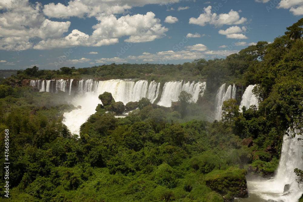 Fototapeta premium The Iguazu falls in the jungle. View of the white falling water flowing across the tropical rainforest in Iguazu national Park, Misiones, Argentina. The waterfalls and lush vegetation.
