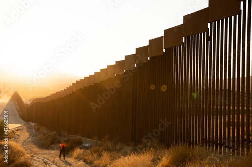 Fototapeta Tecate, Baja California, Mexico - September 14, 2021: Late afternoon sun shines on the USA Mexico border wall people walk in front of it