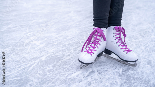 Legs of a girl in white figure skates with purple laces on an outdoor skating rink in the park.