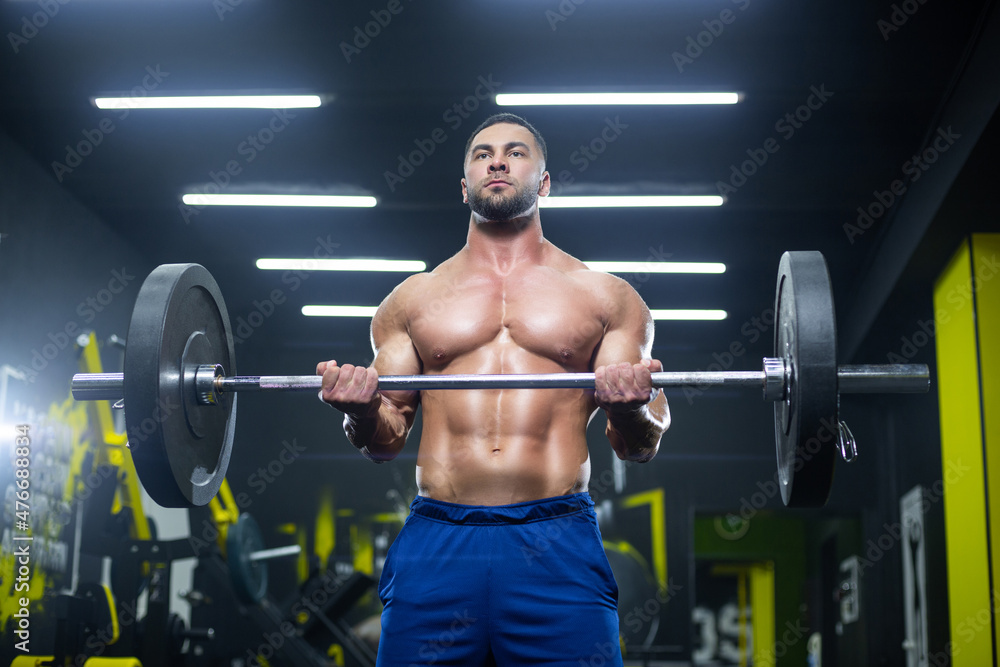 Close up view of a strong muscular athlete lifting heavy barbell showing his muscles in a gym Close up view of a strong muscular athlete lifting heavy barbell showing his muscles in a gym