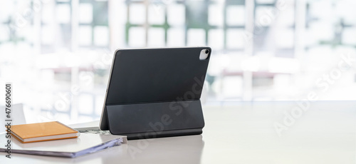 Portable tablet and notebook on wooden table in modern office room with copy space.