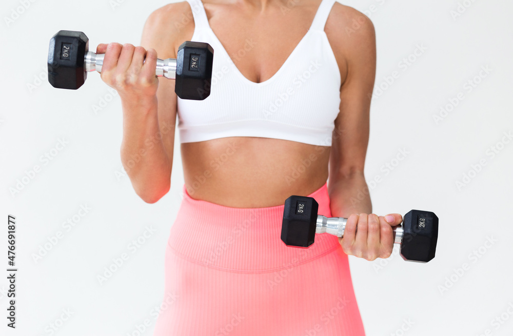 Girl posing with dumbbells in front of a white wall Girl posing with dumbbells in front of a white wall