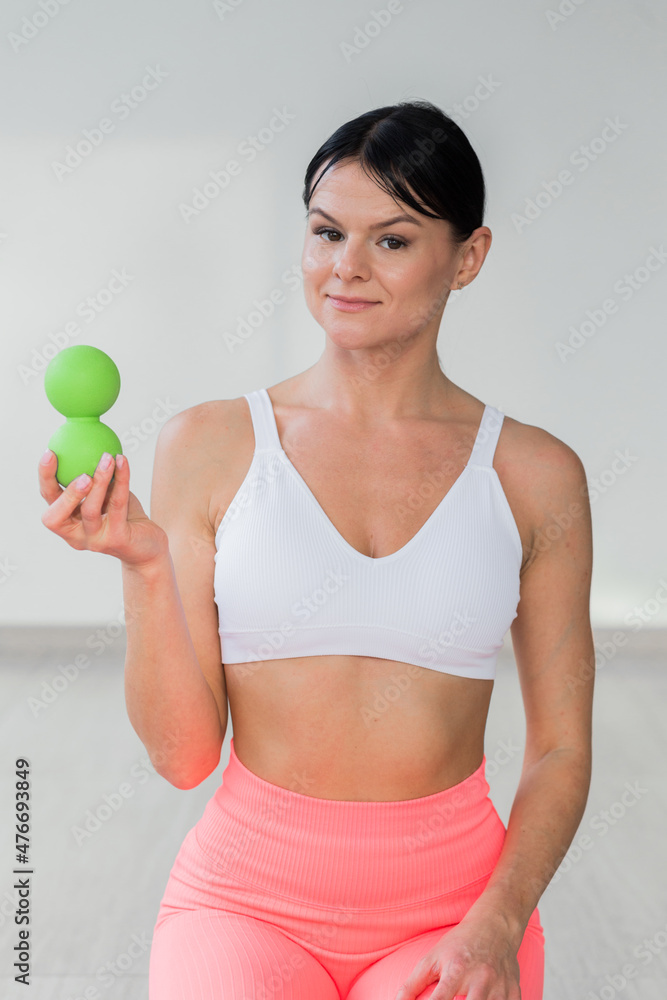 A brunette girl in a white top and coral leggings holds a massage ball in her hands. Ball massager for yoga pilates or stretching and fascia pain. Sports and massage A brunette girl in a white top and coral leggings holds a massage ball in her hands. Ball massager for yoga pilates or stretching and fascia pain. Sports and massage