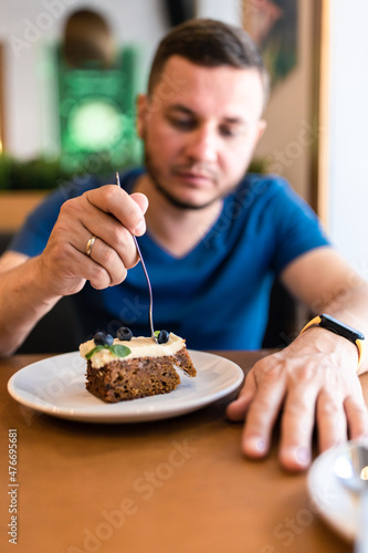 A man eats a cake with blueberries in a cafe. Front view.