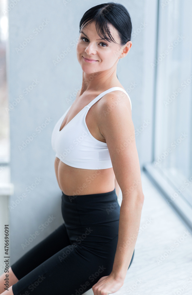 A beautiful brunette girl in a white sports top and black cycling shorts posing near the window and looking at the camera. A beautiful brunette girl in a white sports top and black cycling shorts posing near the window and looking at the camera.