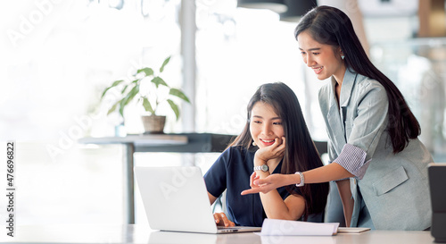 Two young businesswoman meeting and discussing about new business project plan, using computer analyzing financial and marketing with happiness.
