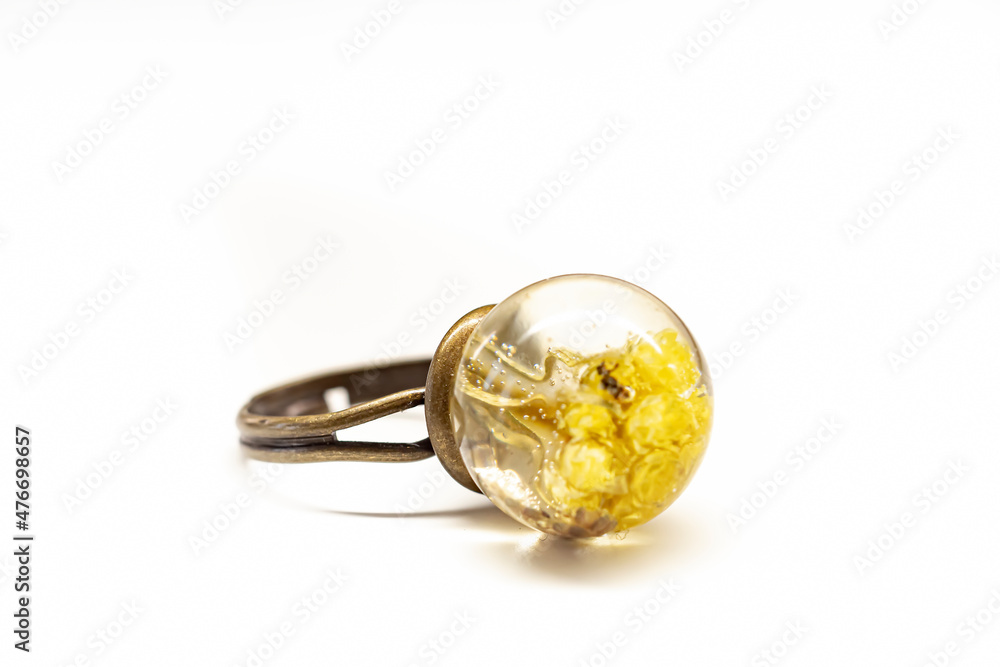 Natural dried plants inside epoxy resin ring. Sphere shaped mold, brass colored metal base, yellow flowers. Selective focus on the details, object isolated on white background. Natural dried plants inside epoxy resin ring. Sphere shaped mold, brass colored metal base, yellow flowers. Selective focus on the details, object isolated on white background.