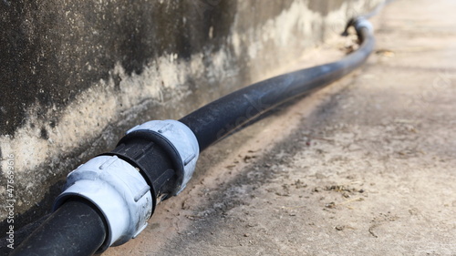 Old HDPE Straight Coupling. Compression fitting straight coupling connects to black plumbing pipe beside concrete wall with copy space. selective focus