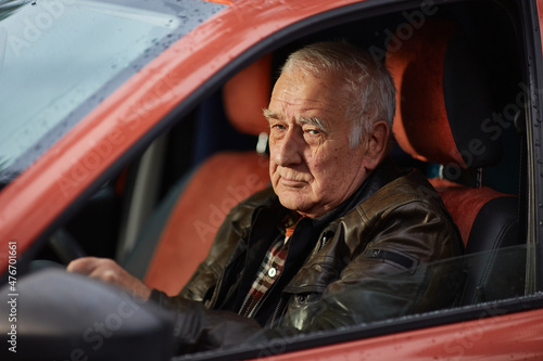 pensioner with gray hair and wrinkles is driving a car.