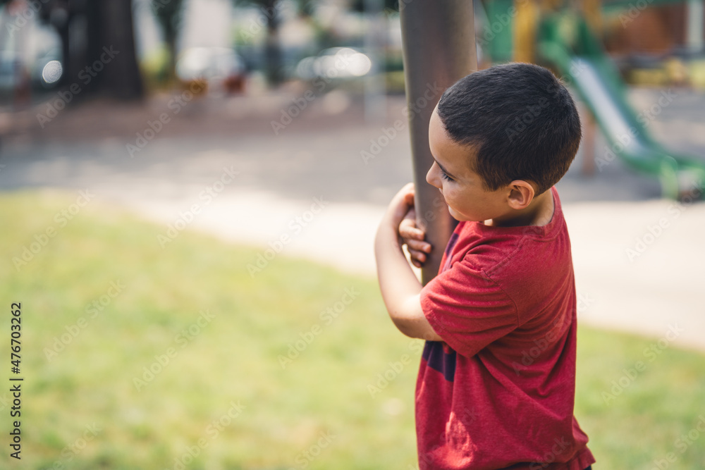 Boy hugs an iron post in the playground and smile while children are swinging Boy hugs an iron post in the playground and smile while children are swinging