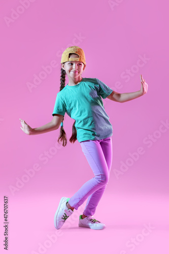 Cute little girl in cap dancing on violet background