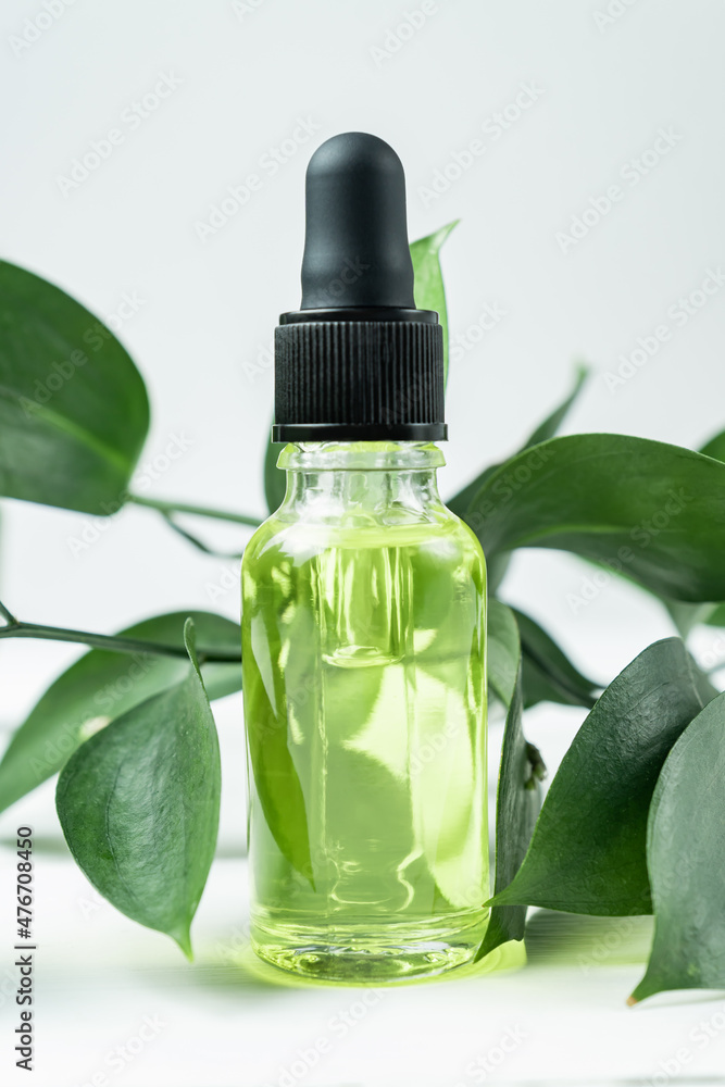 Transparent glass cosmetic bottle with a dropper on a white background with tropical leaves. Natural cosmetics concept, natural essential oil and skin care products Transparent glass cosmetic bottle with a dropper on a white background with tropical leaves. Natural cosmetics concept, natural essential oil and skin care products