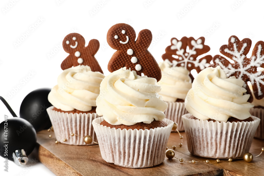 Wooden board of tasty Christmas cupcakes with gingerbread cookies on white background