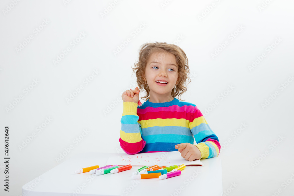 a little cute girl draws at the table with pencils isolated on a white background a little cute girl draws at the table with pencils isolated on a white background