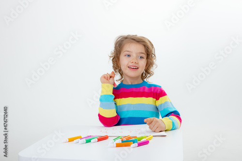 a little cute girl draws at the table with pencils isolated on a white background