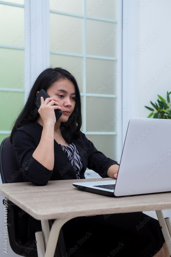 Business woman sitting on chair while making phone call in front of laptop with flat facial expression Business woman sitting on chair while making phone call in front of laptop with flat facial expression
