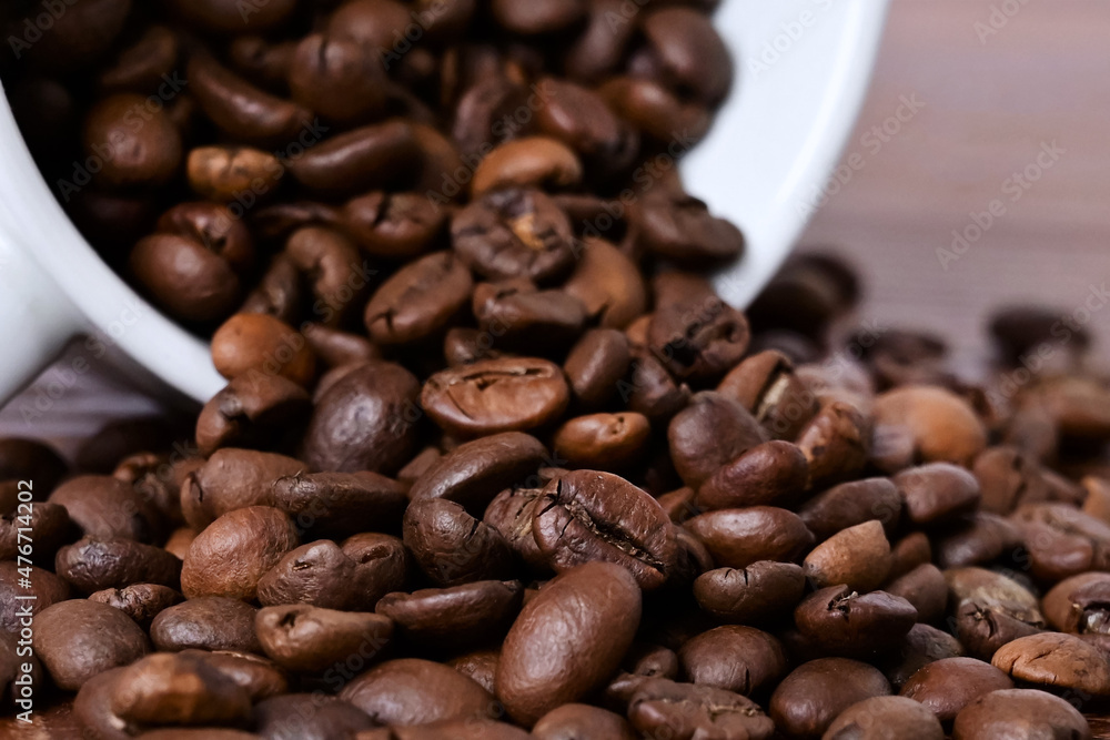 Naklejka premium Coffee beans spill out of a white cup onto a wooden table. Coffee beans on a wooden background. Close-up