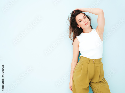 Young beautiful smiling female in trendy summer suit clothes. Sexy carefree woman posing near light blue wall in studio. Positive model having fun indoors. Cheerful and happy