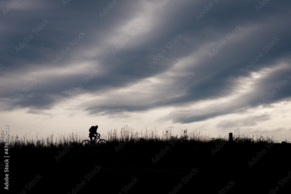 Silhouette of a cyclist on a dike in stormy weather