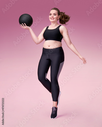 Sporty girl with medicine ball in motion. Photo of model with curvy figure in fashionable sportswear on pink background. Dynamic movement. Sports motivation and healthy lifestyle