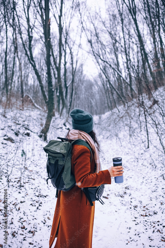 Portrait of a woman in a cap and a winter jacket. She’s drinking a hot tea. Winter time.