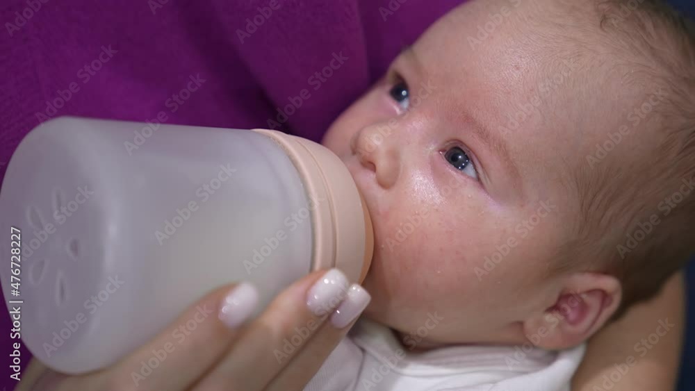 Beautiful sleepy baby suckling milk from a bottle. Mother’s feeding her child holding him in hands. Close up. Beautiful sleepy baby suckling milk from a bottle. Mother’s feeding her child holding him in hands. Close up.