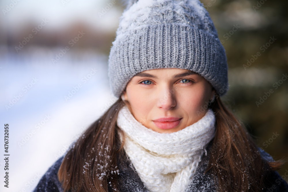 Close up portrait of beautiful attractive girl, young pretty woman looking at camera with serious look in warm clothes hat and scarf standing in winter snowy day outdoors in snow, walking in park. Close up portrait of beautiful attractive girl, young pretty woman looking at camera with serious look in warm clothes hat and scarf standing in winter snowy day outdoors in snow, walking in park.