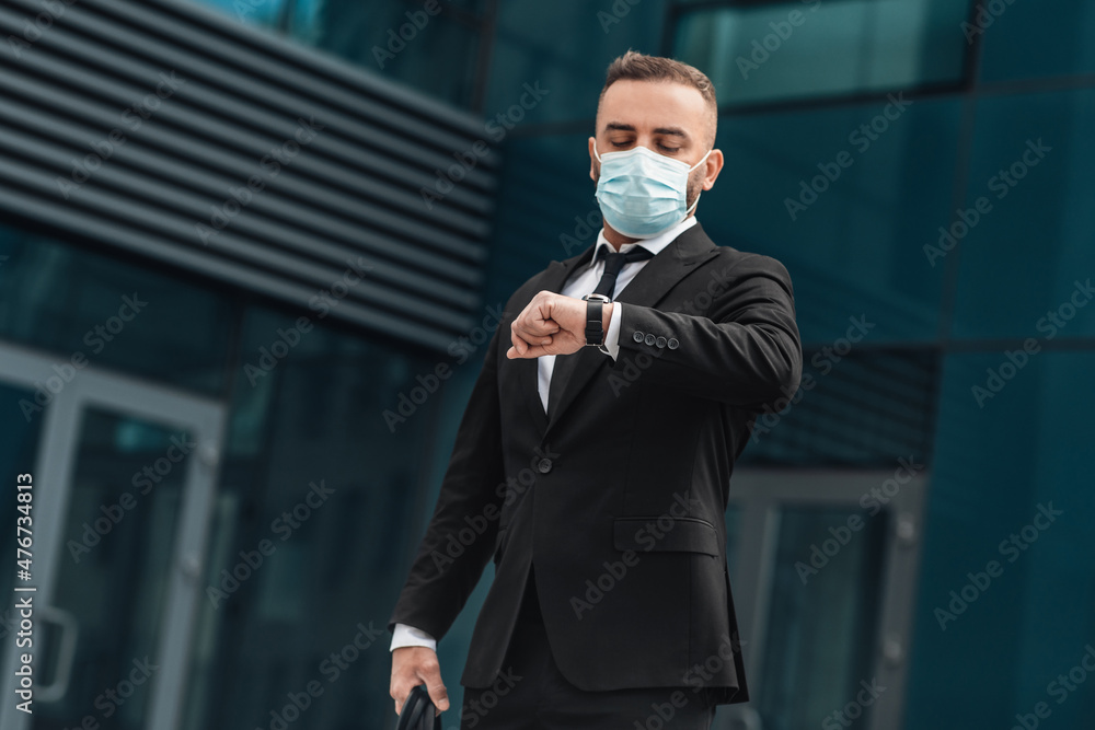 Handsome successful CEO looking at watch for time management, wearing face mask during protect covid-19 virus Handsome successful CEO looking at watch for time management, wearing face mask during protect covid-19 virus