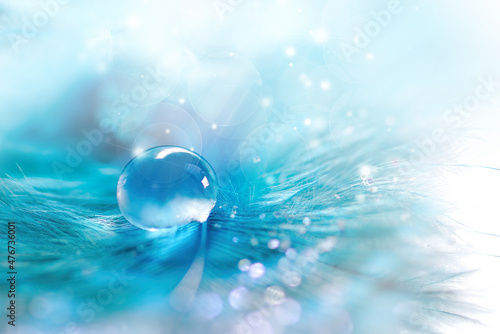 Beautiful drop of water on fluffy feather with sparkling bokeh on light blue blurred background, macro . Abstract romantic delicate magical artistic image purity and fragility of nature.