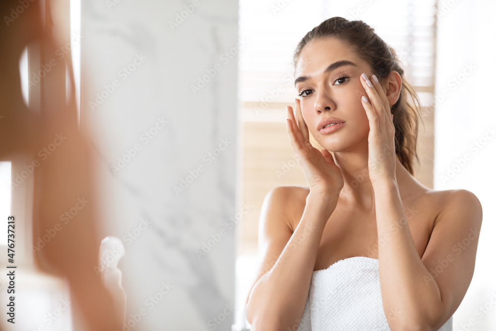 Female Touching Face Looking At Reflection In Mirror In Bathroom Female Touching Face Looking At Reflection In Mirror In Bathroom