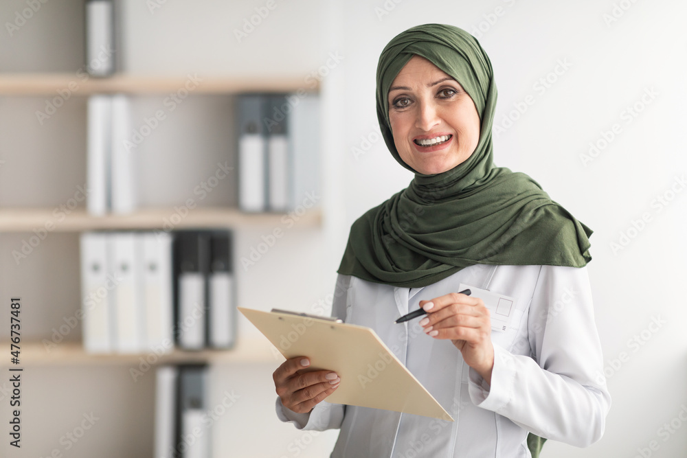 Happy Muslim Female Doctor Posing Standing In Modern Clinic Office Happy Muslim Female Doctor Posing Standing In Modern Clinic Office