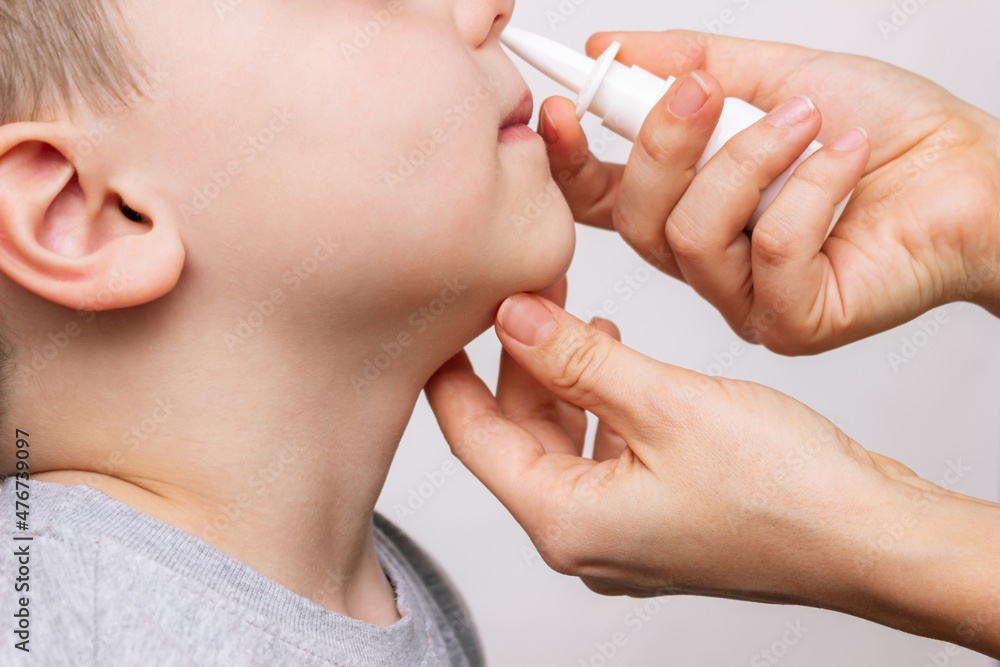 A close-up of female hands using nasal spray for a child's runny nose and congestion isolated on a white background. Treatment of the disease. Rhinitis, sinusitis, cold, flu. A mother treats her kid