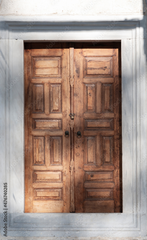 A wooden brown door. Very symmetrical photo. Sun lights hit to door. Architectural elements.
