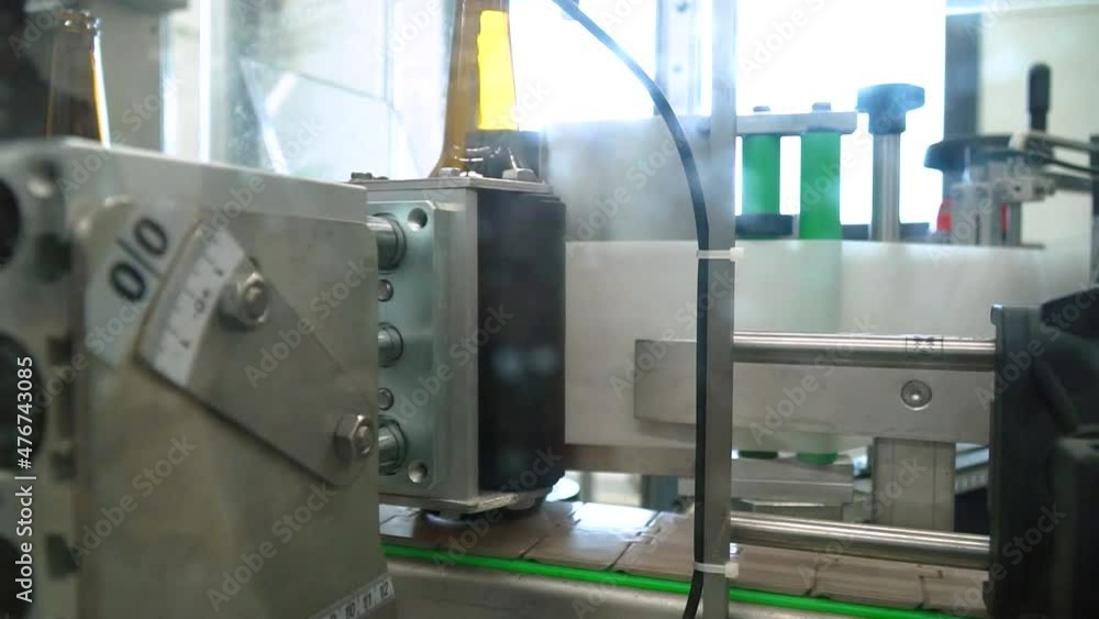 Close Up Of Automatic Labeling Machine At Work With Empty Bottles Moving On Conveyor In A Bottling Factory. Close Up Of Automatic Labeling Machine At Work With Empty Bottles Moving On Conveyor In A Bottling Factory.