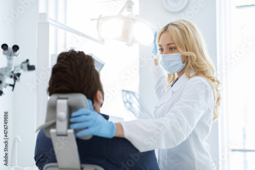 Female dentist turning on lamp  looking at patient