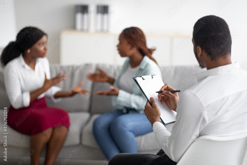Angry LGBT lesbian couple having quarrel during session with marital counselor, arguing with each other Angry LGBT lesbian couple having quarrel during session with marital counselor, arguing with each other