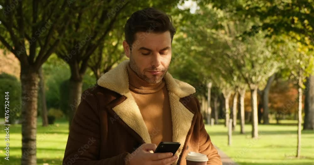 Handsome young man having coffee and using mobile phone. male using phone and drink tea in the city Park. a man in a brown jacket is drinking coffee in park and is wait for his girlfriend for a date Handsome young man having coffee and using mobile phone. male using phone and drink tea in the city Park. a man in a brown jacket is drinking coffee in park and is wait for his girlfriend for a date
