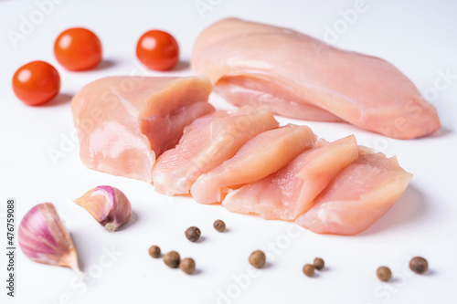 Raw chicken breast, chicken fillet cut into slices with garlic, cherry tomatoes and pepper side by side, isolated on a white background