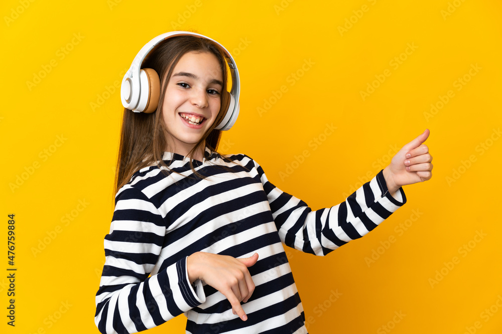 Little girl isolated on yellow background listening music and doing guitar gesture