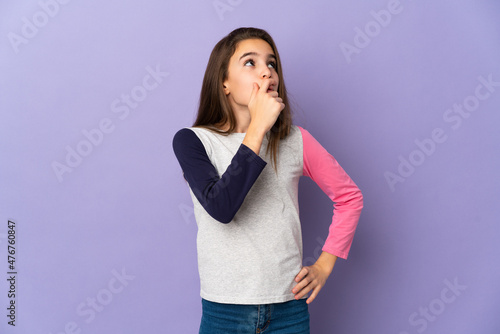 Little girl isolated on purple background having doubts and with confuse face expression