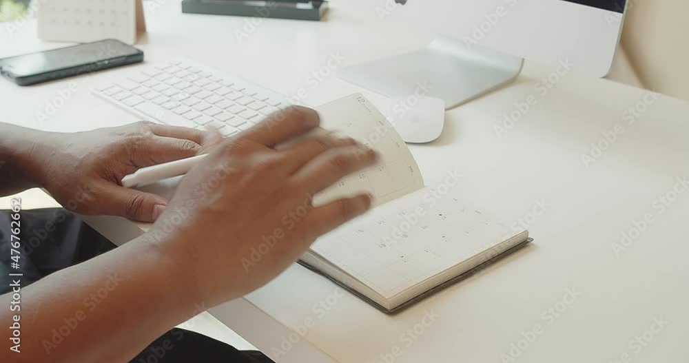 Close up Asian hand businessman holding a pen making notes in personal paper planner at desk Close up Asian hand businessman holding a pen making notes in personal paper planner at desk