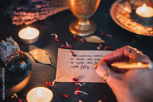 Female woman writing a note in a cursive handwriting with a fancy gold fountain pen. Golden pen nib, Black ink on aged old paper. Candle light mood, cozy dark academia aesthetic. 