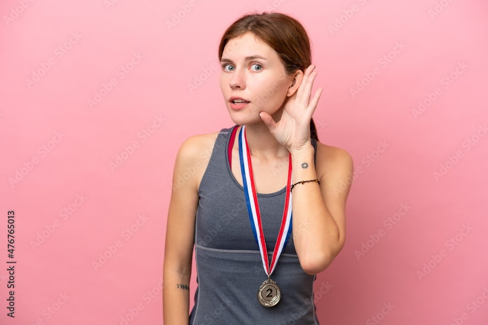 Young English woman with medals isolated on pink background listening to something by putting hand on the ear Young English woman with medals isolated on pink background listening to something by putting hand on the ear