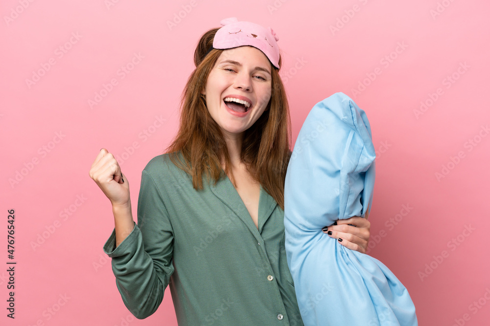Young English woman in pajamas isolated on pink background in pajamas and holding a pillow and celebrating a victory Young English woman in pajamas isolated on pink background in pajamas and holding a pillow and celebrating a victory
